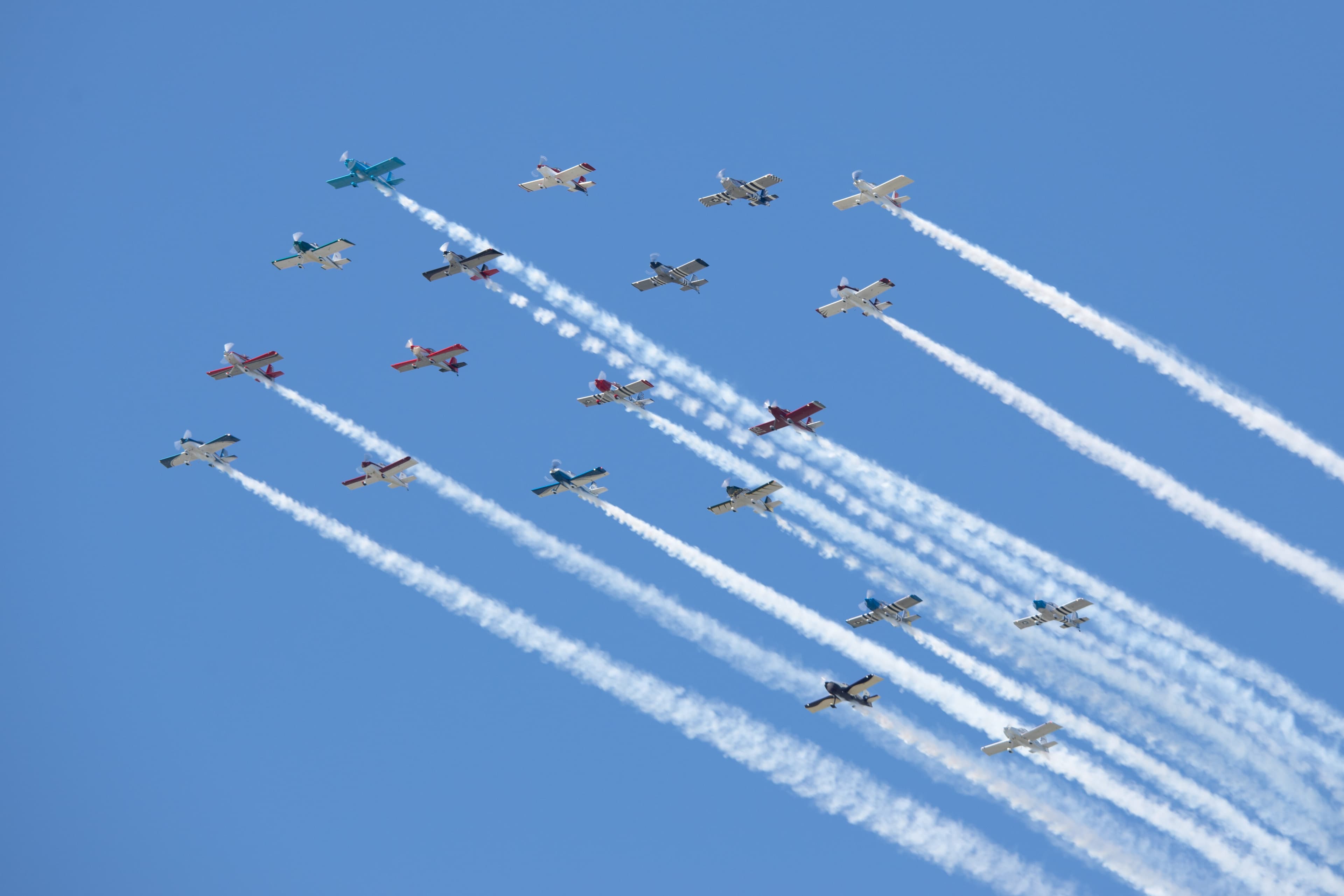 Aircraft in formation trailing smoke against a blue sky at AirVenture
